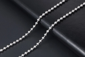 Detail of polished silver stainless steel ball chain on a black leather background