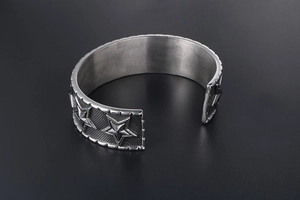 Close-up of vintage pentagram engraving on wide open-cuff punk steel bracelet