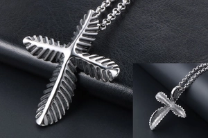 Macro detail of silver stainless steel cross pendant with textured leaf patterns and link chain