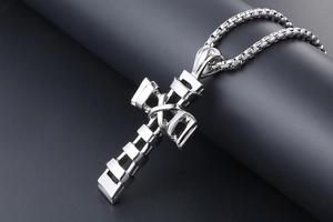 Macro shot of a layered silver cross pendant with metallic box chain on grey stone surface