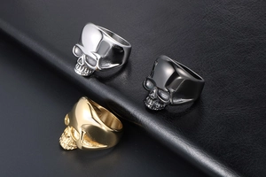 Detailed view of skull rings in silver, black and gold finishes on a textured leather background