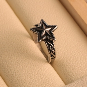 Detail of vintage star ring in titanium steel with intricate embossed scrolls on a beige box