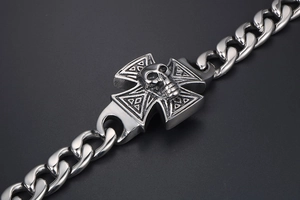 Detailed view of punk skull emblem and iron cross charm on silver steel curb chain bracelet