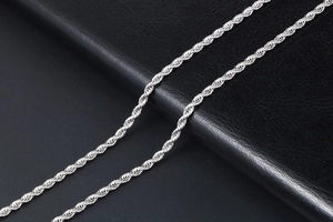 Close-up of a silver stainless steel rope chain necklace on black leather background