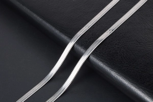 Macro detail of silver flat snake chain with polished metal texture on black leather