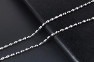Macro shot of silver oval bead titanium steel chain on black leather surface