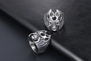 Close-up of gothic silver skull rings with wing carvings on black leather background