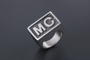 Macro shot of silver signet ring with embossed MC letters on textured black background