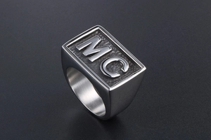 Close-up of industrial style men's signet ring with embossed MC letters on steel band