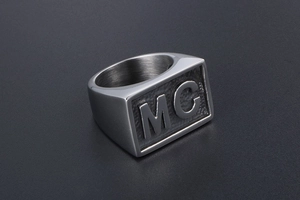 Macro detail of silver signet ring featuring embossed MC letters on a textured surface