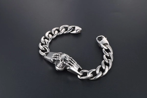 Détail d'un bracelet punk en acier titane avec motif de crâne et mains squelettiques
