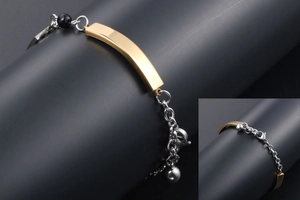 Detail of polished gold curved plate on silver stainless steel bracelet with black bead