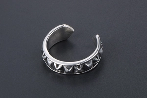 Close-up of silver punk ear cuff featuring edgy pyramid rivets and brushed metal texture