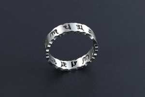 Gros plan d'une bague en acier titane argenté aux bords ondulés et mantras gravés