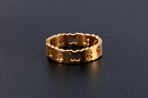 Vue détaillée d'une bague en acier doré avec bords ondulés et motifs de caractères évidés