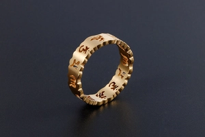 Gros plan sur une bague en titane dorée avec mantra évidé et bords ondulés ciselés
