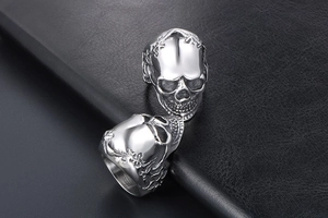 Close-up of two polished titanium steel skull rings with floral details on black leather