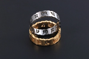 Détail de bagues en acier brossé or et argent avec mantras évidés et bordure ondulée