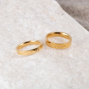 Titanium steel couple rings in gold finish engraved with Forever Love on stone surface