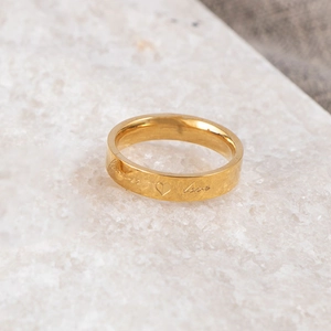 Macro detail of golden ring with Forever Love engraving and heart symbol on marble