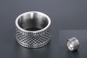 Détail d'une bague large en acier titane avec motif quadrillé et bordures perlées