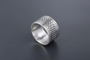 Vue macro d'une bague large en acier titane avec motif de grille vintage et bords perlés