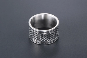 Vue macro d'une bague large en acier avec motif à losanges et bords perlés détaillés