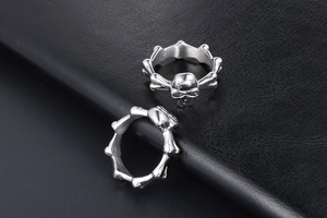 Close-up of silver punk skull rings with bone-shaped bands on black leather background