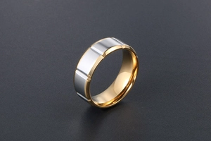 Détail d'une bague bicolore en acier titane style industriel sur surface de sable noir