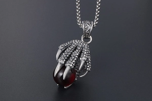 Close-up of vintage steel dragon claw pendant with deep red crystal bead and silver chain