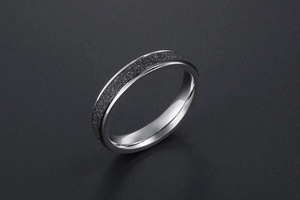 Détail d'une bague aux bords argentés avec insert noir mat sur fond gris texturé