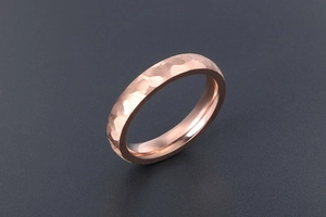 Close-up of rose gold ring featuring unique hammered texture on a dark grey background