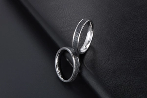 Détail de bagues de couple en acier noir mat et argent poli sur fond de cuir