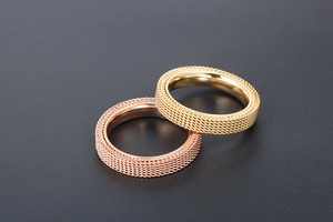 Detail of woven mesh texture on gold and rose steel rings with polished inner surface