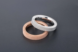 Detail of silver and rose gold mesh textured titanium steel rings on dark surface