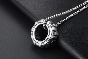 Macro d'un pendentif pneu en argent avec chaîne box sur un fond de cuir noir