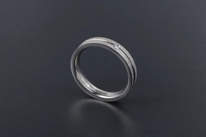Macro detail of matte titanium steel ring with a single inset crystal and engraving