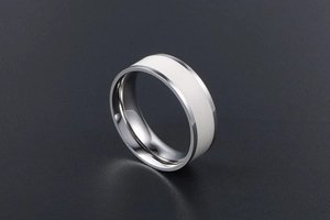 Macro detail of polished stainless steel ring with wide white ceramic inlay on dark surface