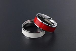 Close-up of polished stainless steel rings with red and white enamel bands on dark background