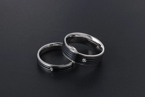 Gros plan de bagues de couple en acier titane avec rayures noires et petit diamant