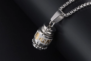 Macro shot of stainless steel mantra pendant with gold-toned prayer bottle details