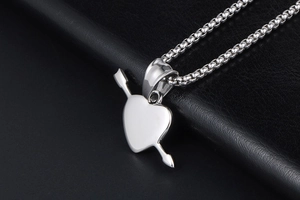 Close-up of polished stainless steel heart and arrow pendant on black leather background