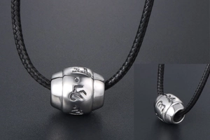 Close-up of vintage titanium steel barrel bead pendant with engraved Buddhist mantra symbols