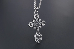 Close-up of silver gothic cross pendant with embossed floral patterns on a box chain