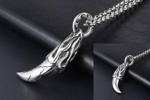 Detailed view of silver wolf tooth pendant with flame carvings and vintage steel texture