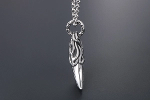 Macro detail of men's wolf tooth pendant with polished flame carvings on steel