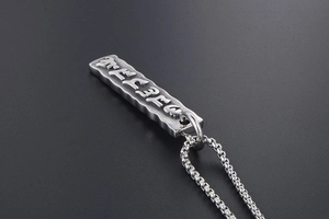 Macro detail of silver stainless steel rectangular pendant with embossed mantra engraving