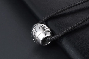 Close-up of a silver cylinder pendant with engraved characters on a black leather surface