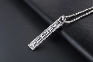 Macro detail of men's titanium steel rectangle pendant with engraved mantra symbols