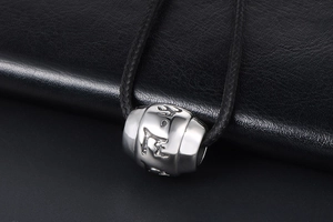 Macro shot of silver titanium steel mantra barrel bead with black braided cord